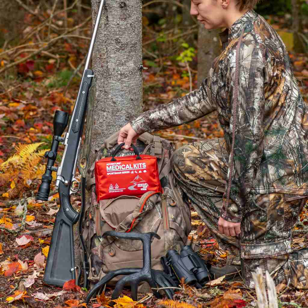 Sportsman Series Medical Kit - 200 hunter holding kit on backpack with gun next to her