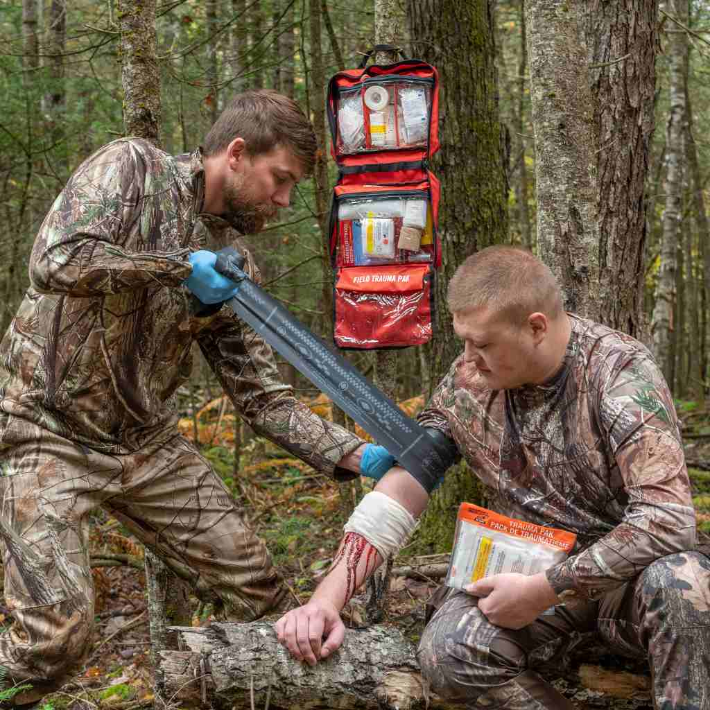 Sportsman Series Medical Kit - 400 man wrapping a tourniquet around friend's arm with kit hanging in background