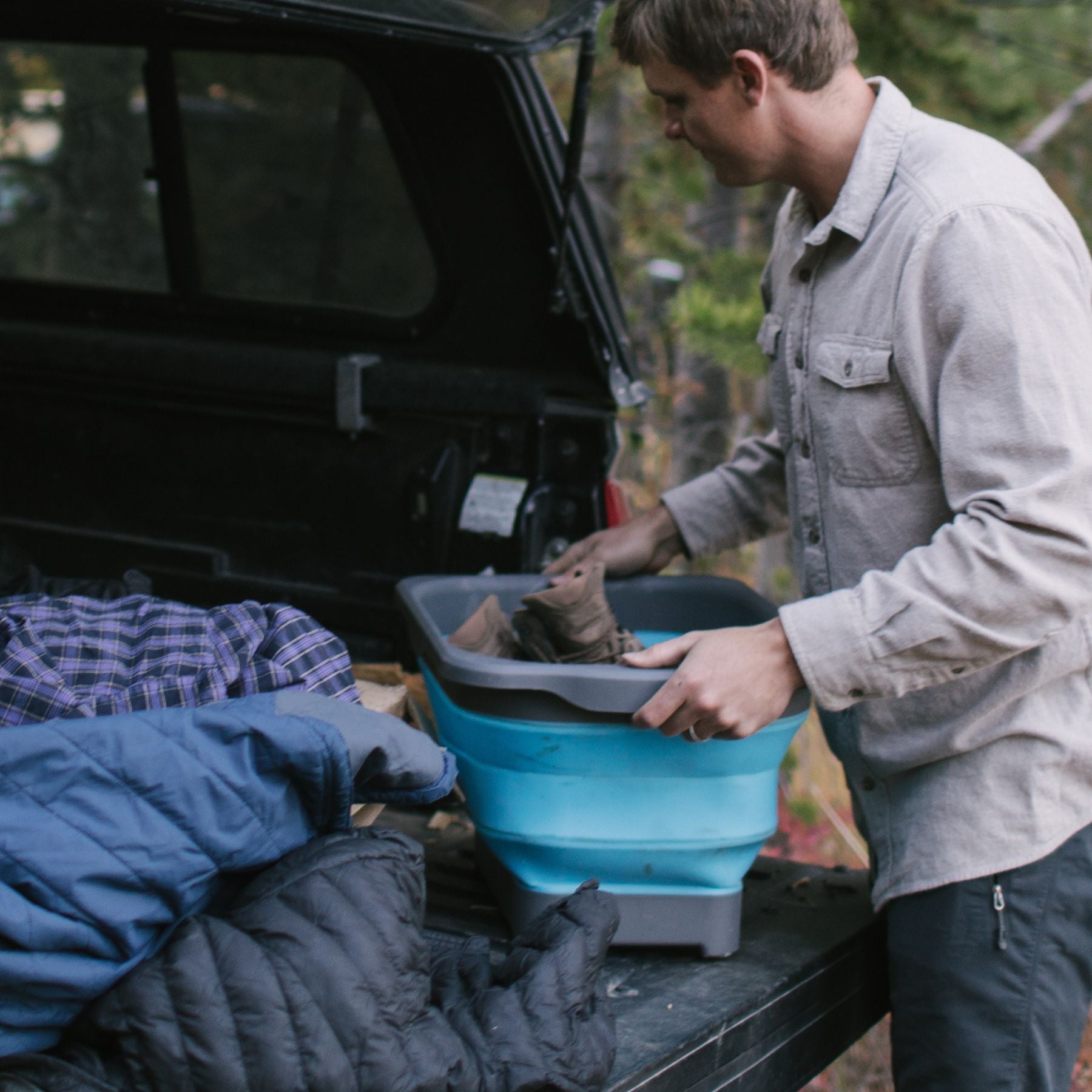 Man Putting SOL Flat Pack Collapsible Gear Tub Into Back of Truck with Blankets and Sleeping Bags