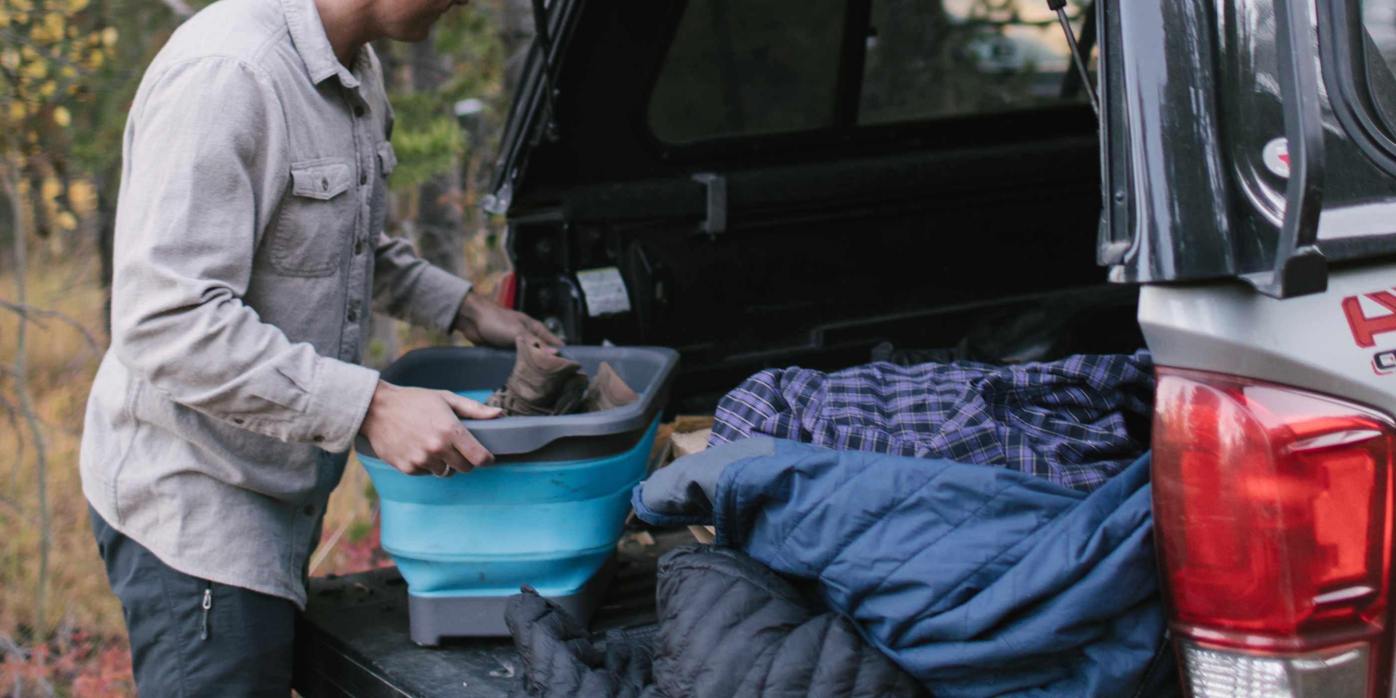 Man Putting SOL Flat Pack Collapsible Gear Tub Into Back of Truck with Blankets and Sleeping Bags